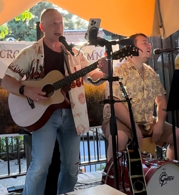 Crossing Autumn, an acoustic duo, playing live: one singing with an acoustic guitar, the other singing at a drum kit